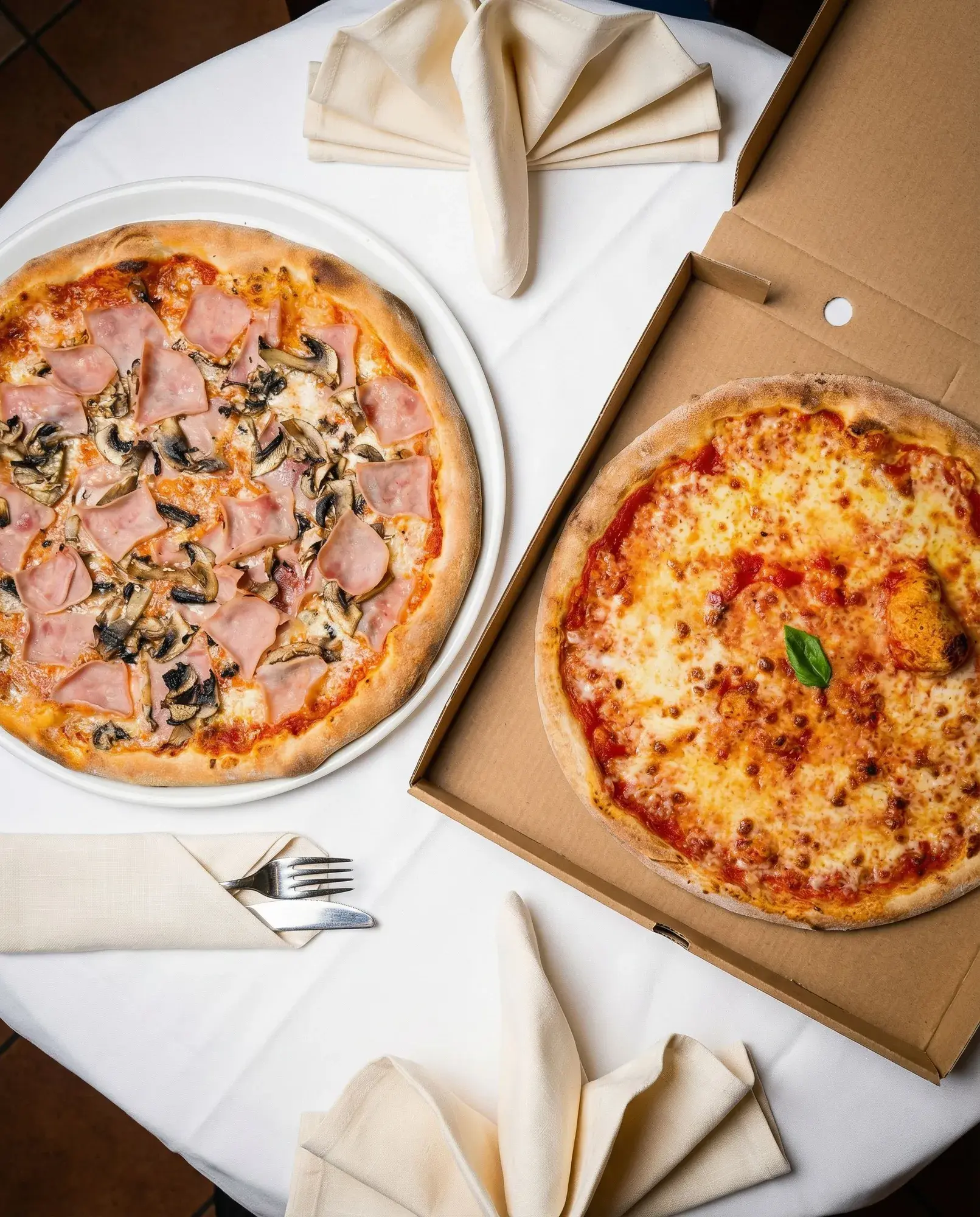 Pizza am Teller neben einer Pizza im Karton für zu Hause bei La Commedia.
